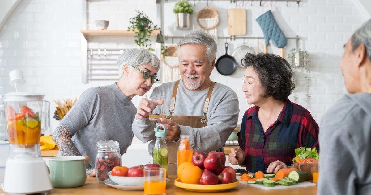 People smiling as they stand around a table full of produce while taking a cooking class.