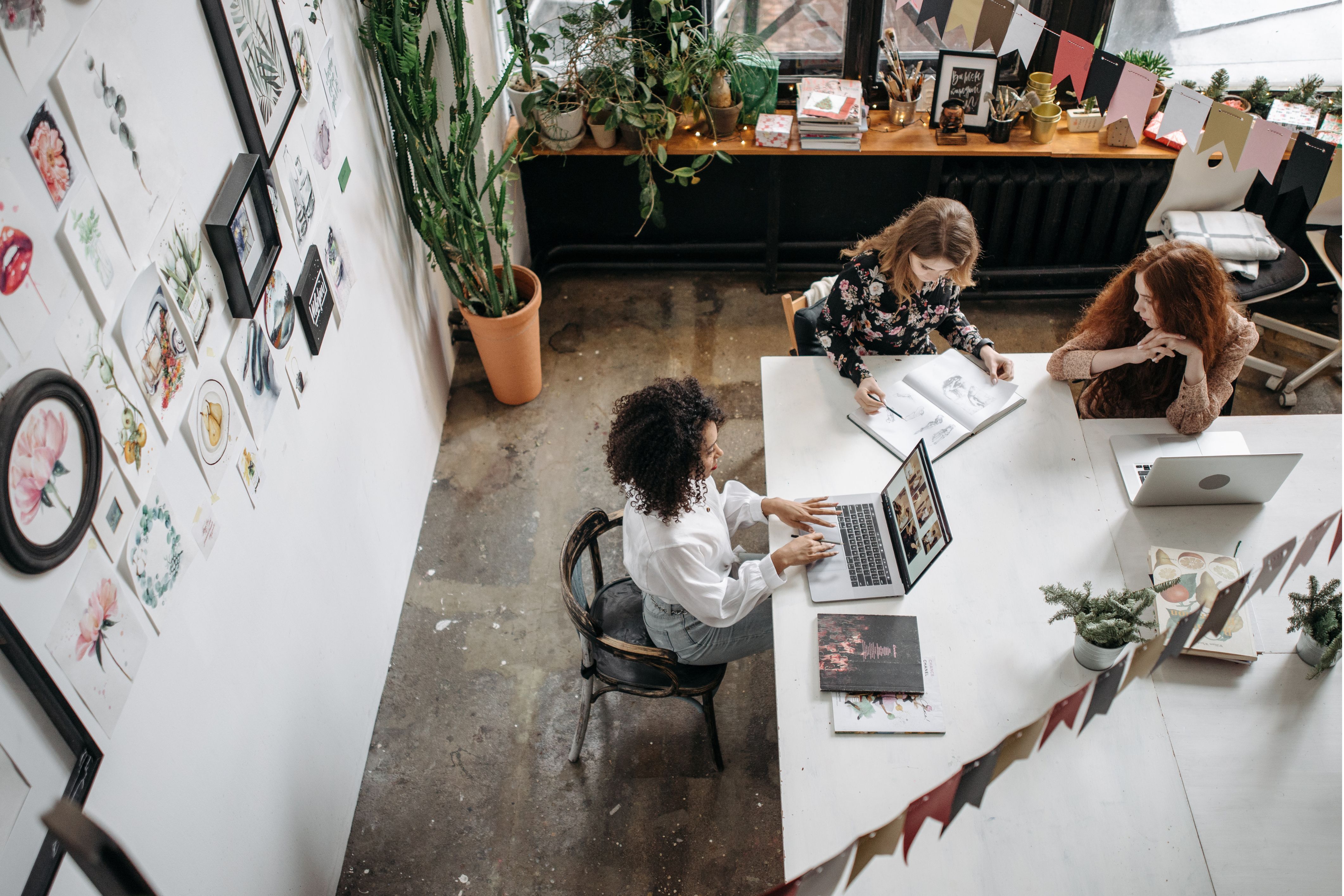 High-angle view of three marketing professionals in a design office. One works alone on a computer, while the other two are in a creative meeting to develop new ideas.