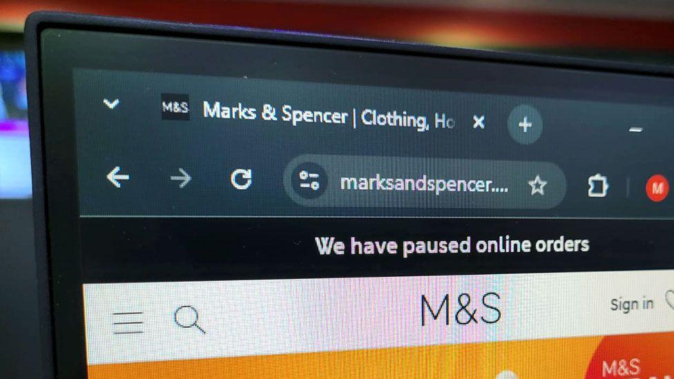 A close-up photo of the Marks and Spencer website shows a black banner with white font informing visitors: 